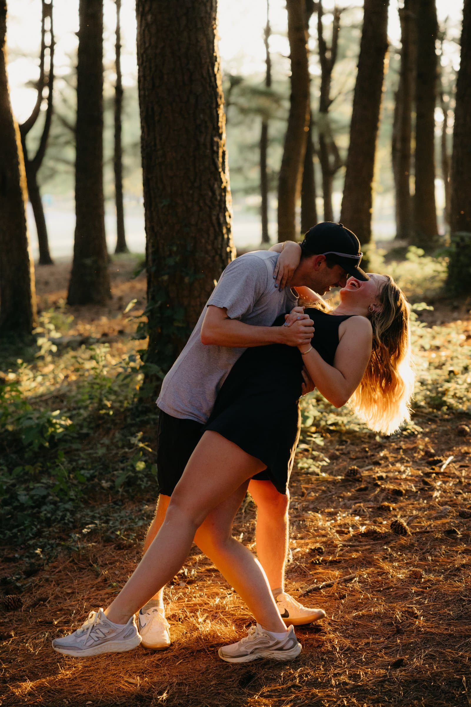 A couple dipped into a kiss with the sun flaring through the pines